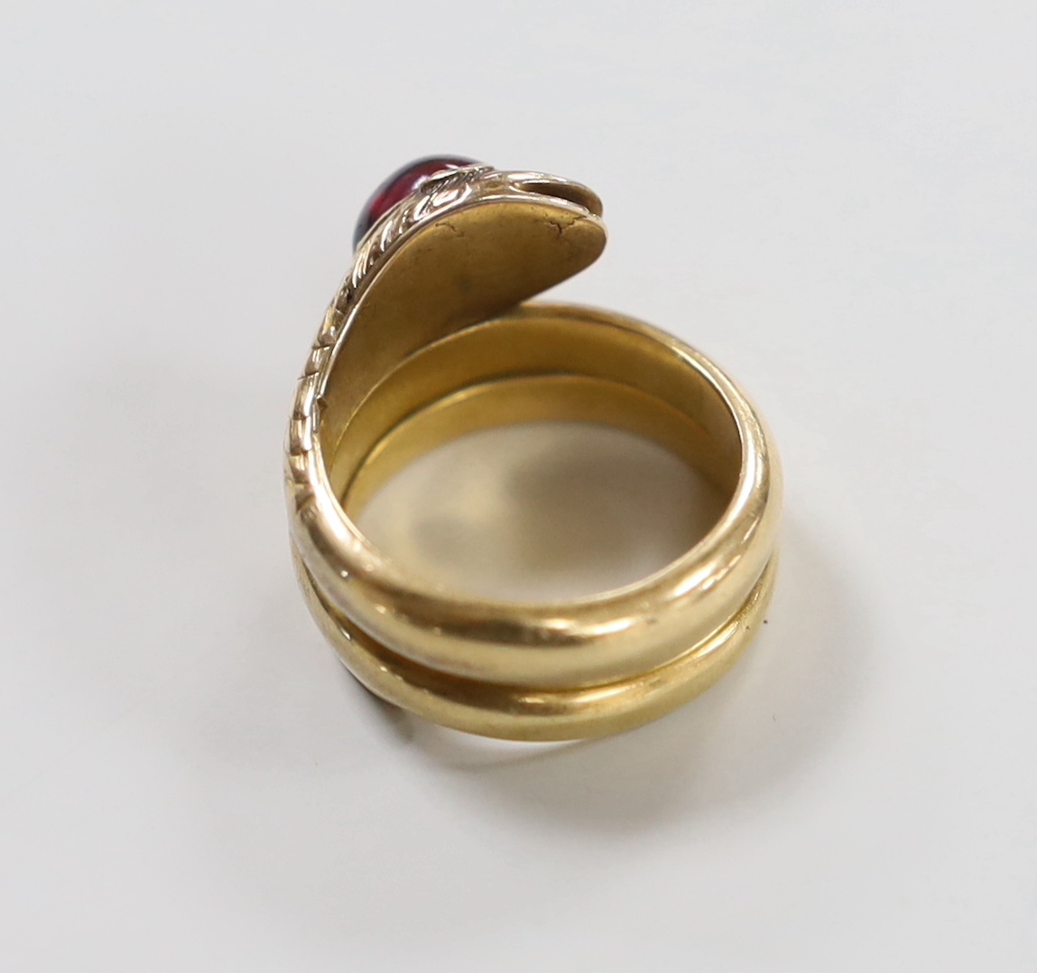 A yellow metal and garnet set coiled serpent ring, with diamond chip eyes, size P, gross weight 15 grams.